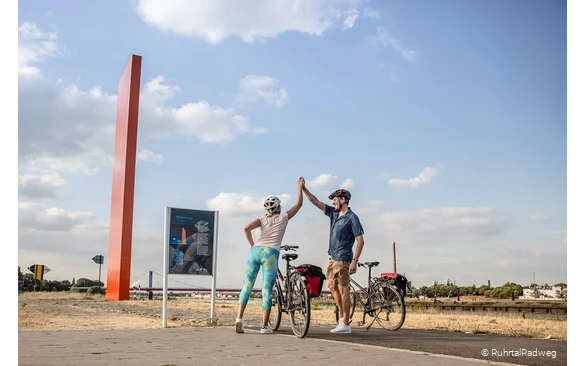 Radfahrer klatschen sich am Ziel des RuhrtalRadwegs, der Rheinorange in Duusburg, ab