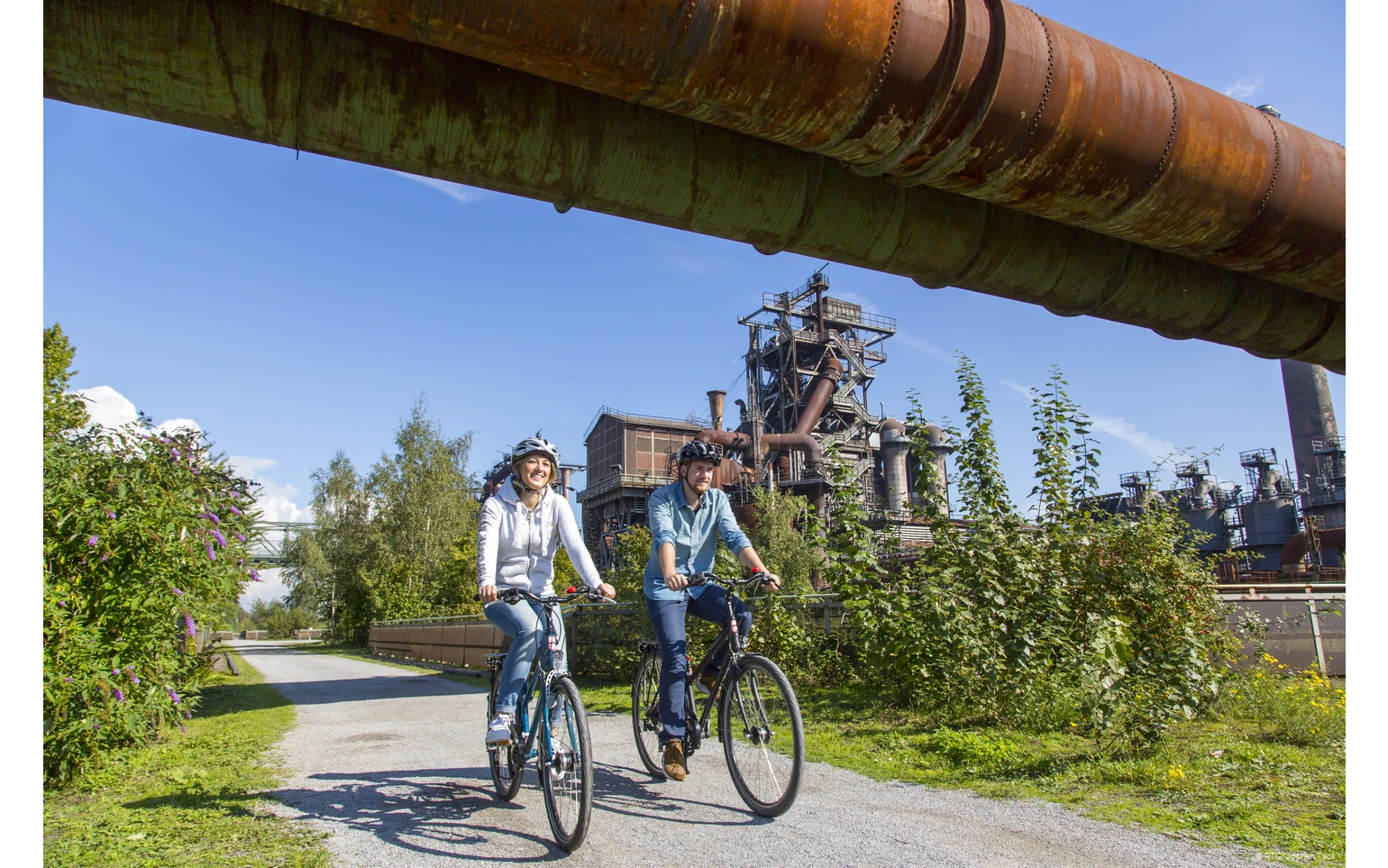 ruhrtalradweg-radrevier-duisburg Zwei Radfahrer im Landschaftspark Duisburg bei blauem Himmel.