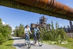 Zwei Radfahrer im Landschaftspark Duisburg bei blauem Himmel.